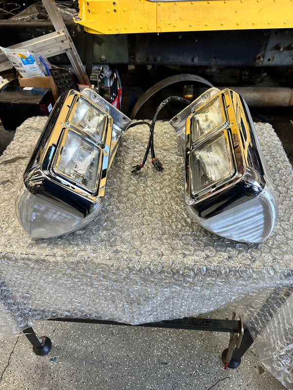 Pair of chrome heavy duty truck headlights with wiring on a bubble-wrapped table in workshop