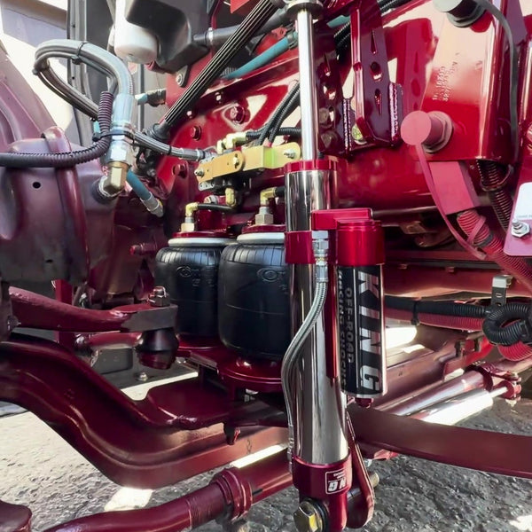 A close-up of a red and silver Nitec hydraulic shock absorber mounted on a red mechanical frame, with hoses and other machinery components visible in the background.