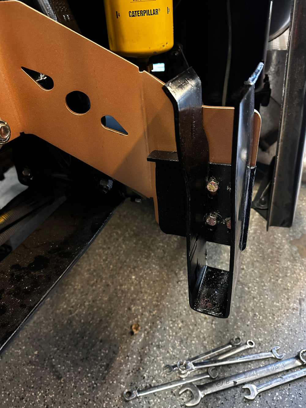 Heavy duty truck suspension component with yellow Caterpillar part and wrenches on floor