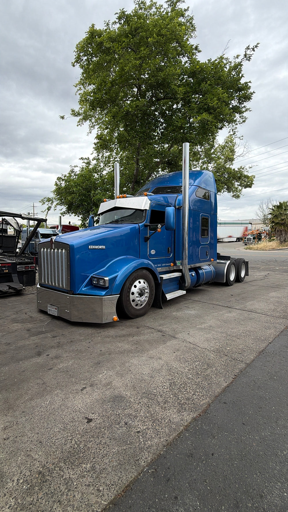 Blue semi-truck parked on a paved road with trees in the background