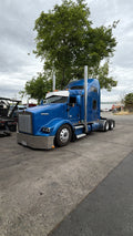 Blue semi-truck parked on a paved road with trees in the background