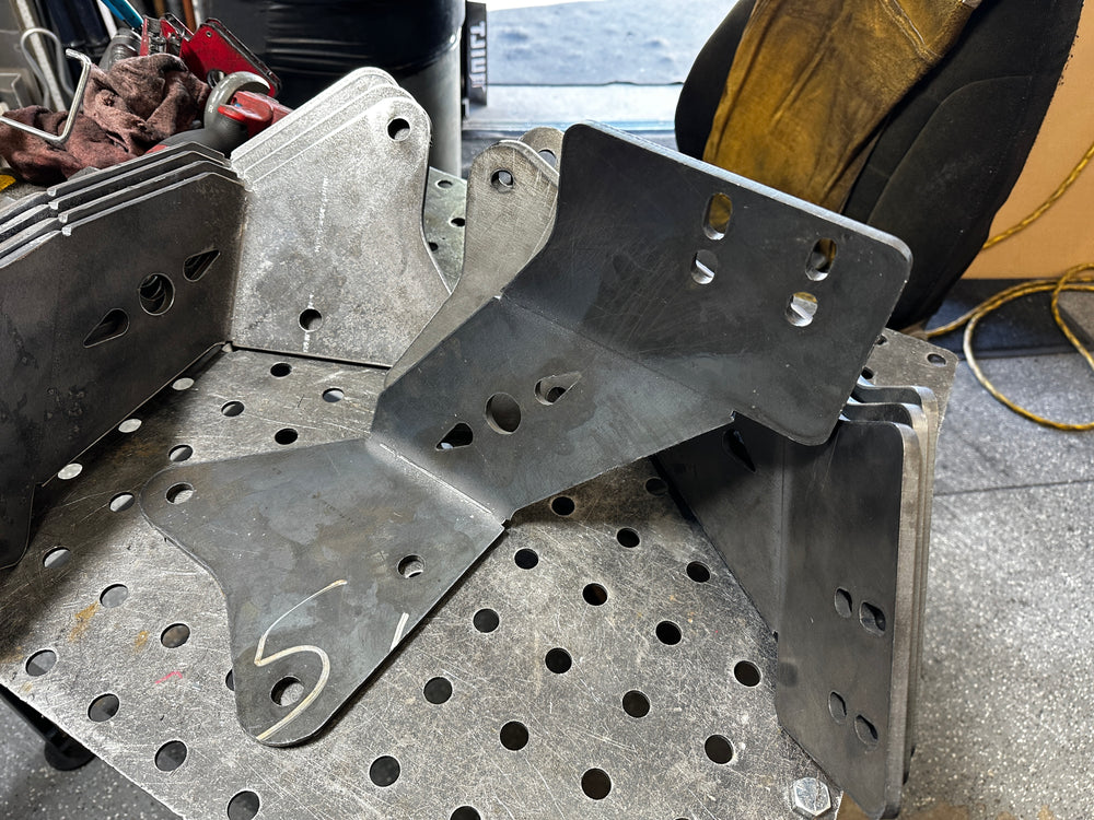 Heavy duty steel truck brackets on a metal workbench, custom fabricated with mounting holes.