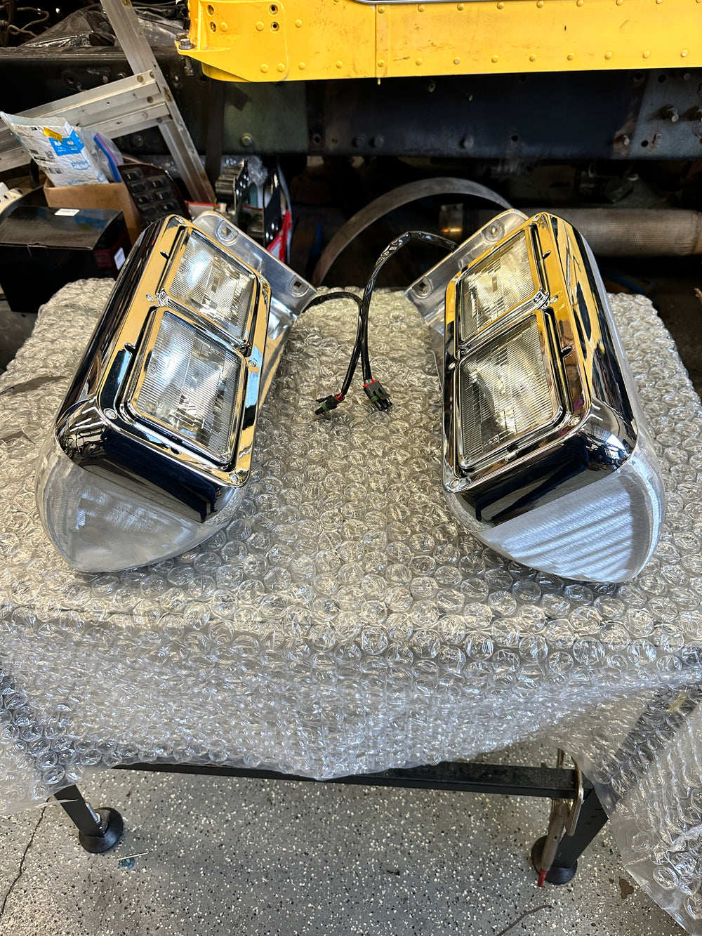 Pair of chrome heavy duty truck headlights with wiring on a bubble-wrapped table in workshop