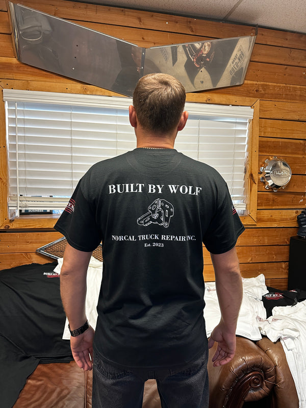 Man wearing black Built By Wolf NorCal Truck Repair T-shirt in rustic office with wood walls.