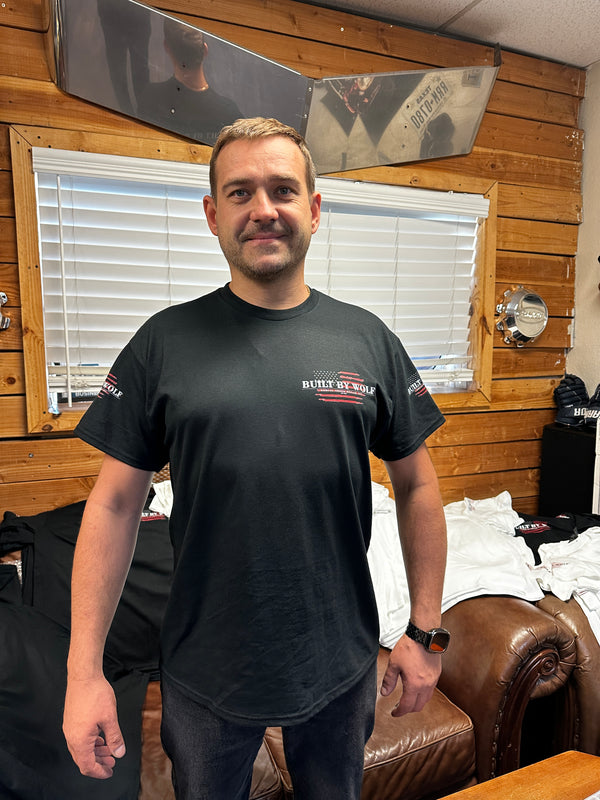 Man wearing black Built By Wolf t-shirt inside wood-paneled truck repair shop