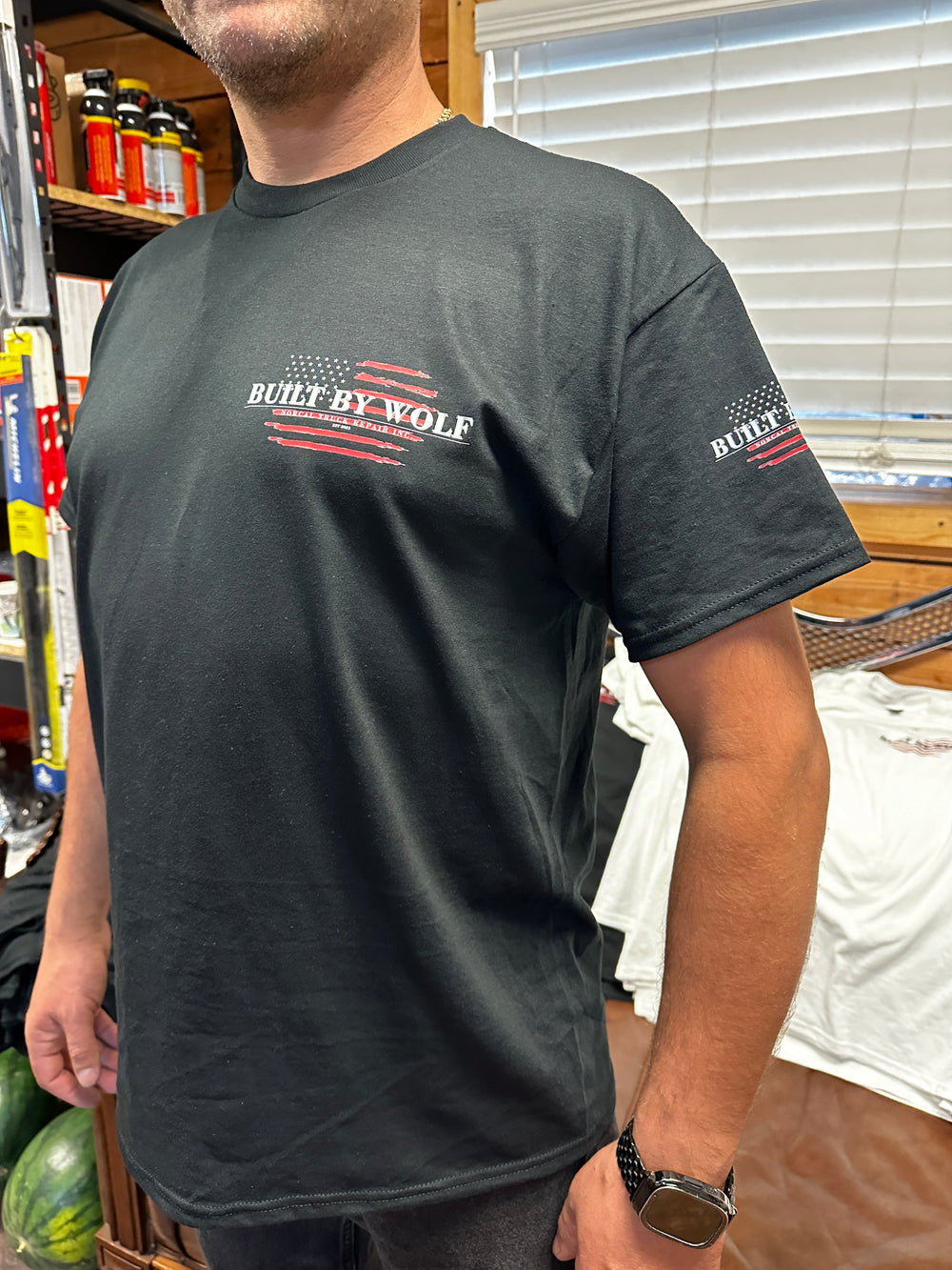 Man wearing black t-shirt with Built By Wolf logo, American flag graphic, shop setting