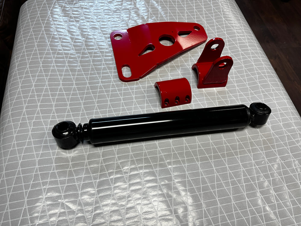 Heavy duty truck suspension parts, black shock absorber and red metal brackets on a table.