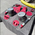 A set of used automotive suspension parts, including two silver coilover bumpers, a shock absorber, and red plastic shims and brackets, displayed on a black textured tablecloth with a red truck in the background.