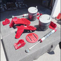 A set of red and silver suspension and shock absorber parts arranged on a gray textured mat outdoors on pavement.