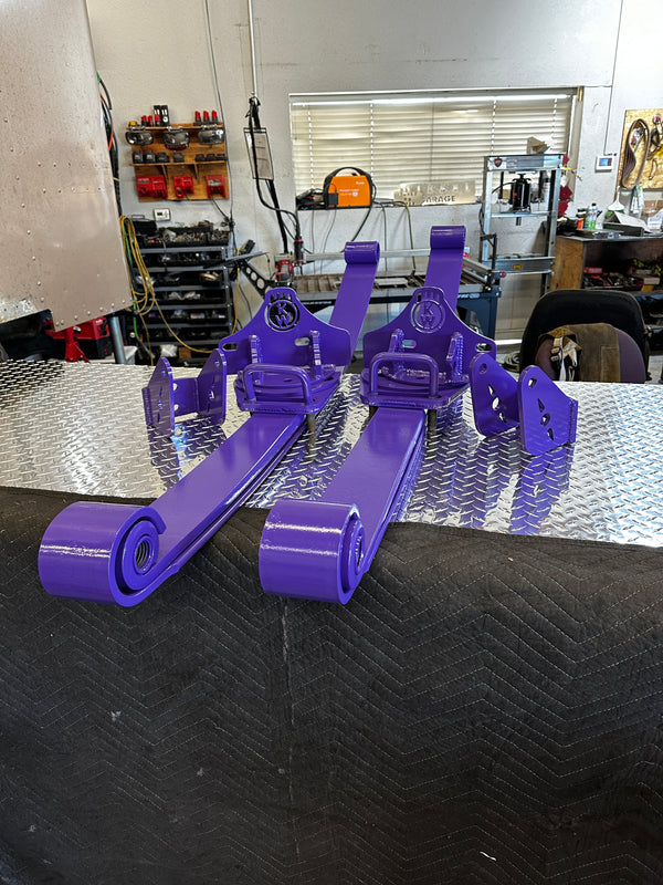 Purple heavy duty custom truck suspension brackets and leaf springs on workbench in garage.